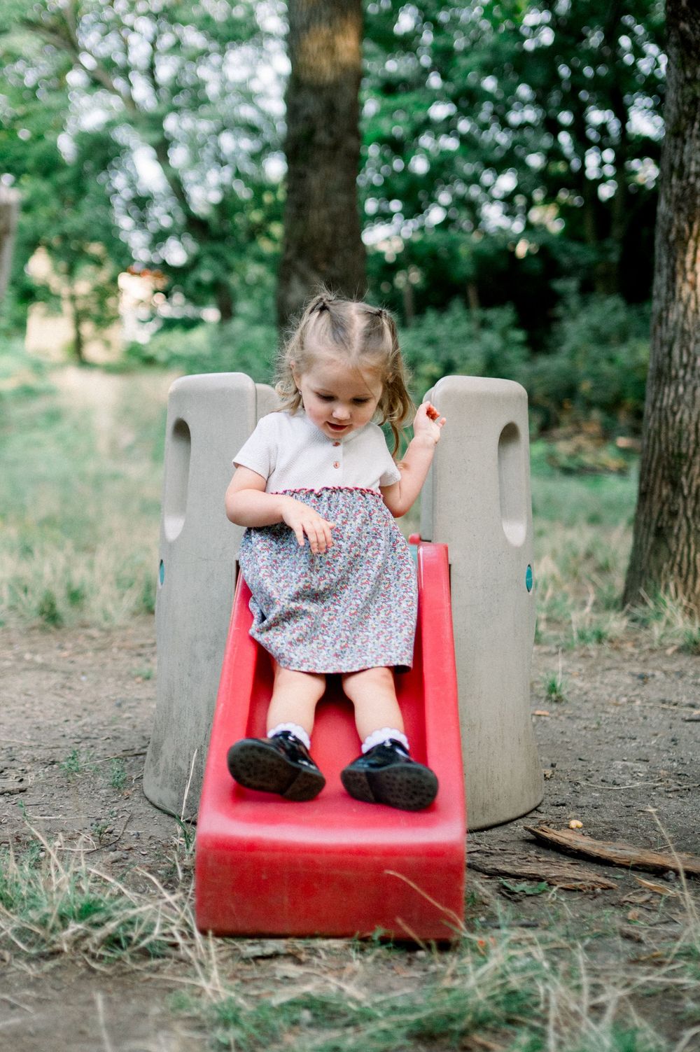 Child playing on a red plastic slide against a woodland backdrop.
