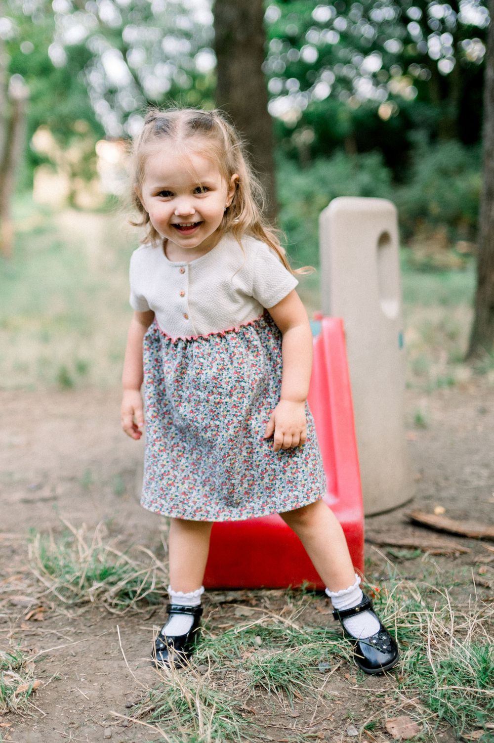 Small child in a floral dress and mary jane shoes playing outdoors.