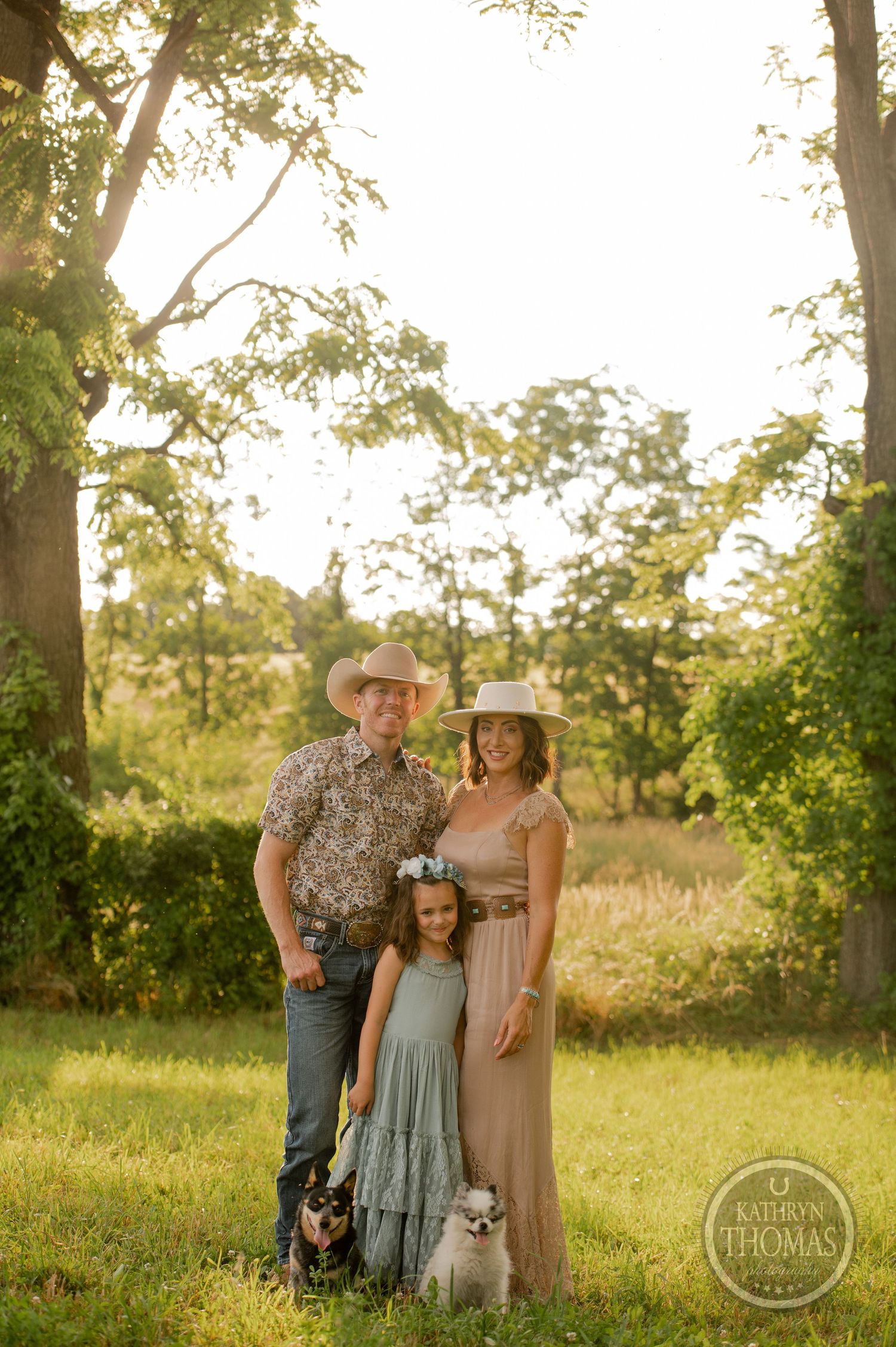 Sunset family photo with two small dogs, western wear, and natural landscape backdrop.