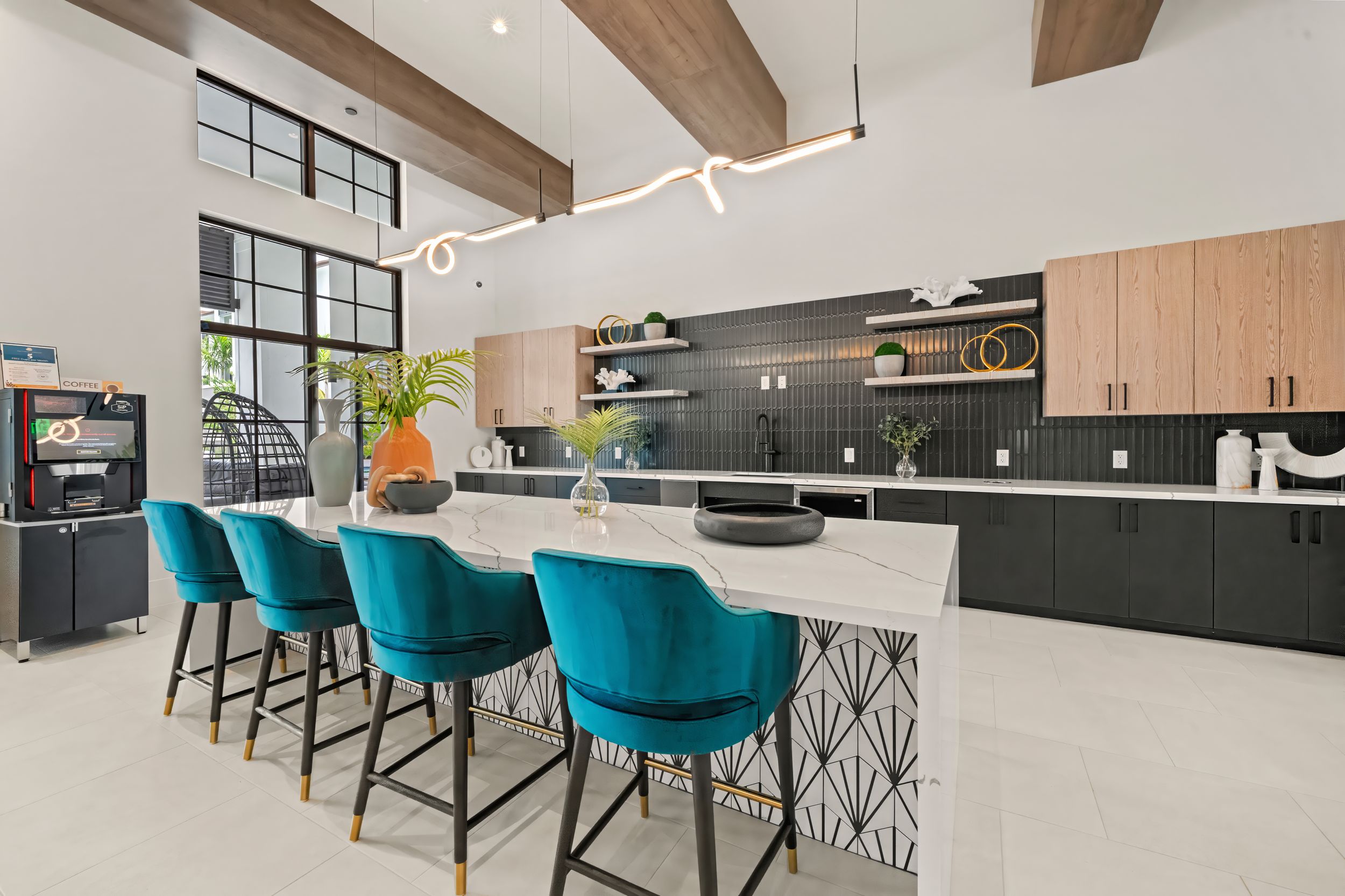 Modern kitchen design featuring teal velvet bar stools and black cabinets with light wood accents and exposed ceiling beams.