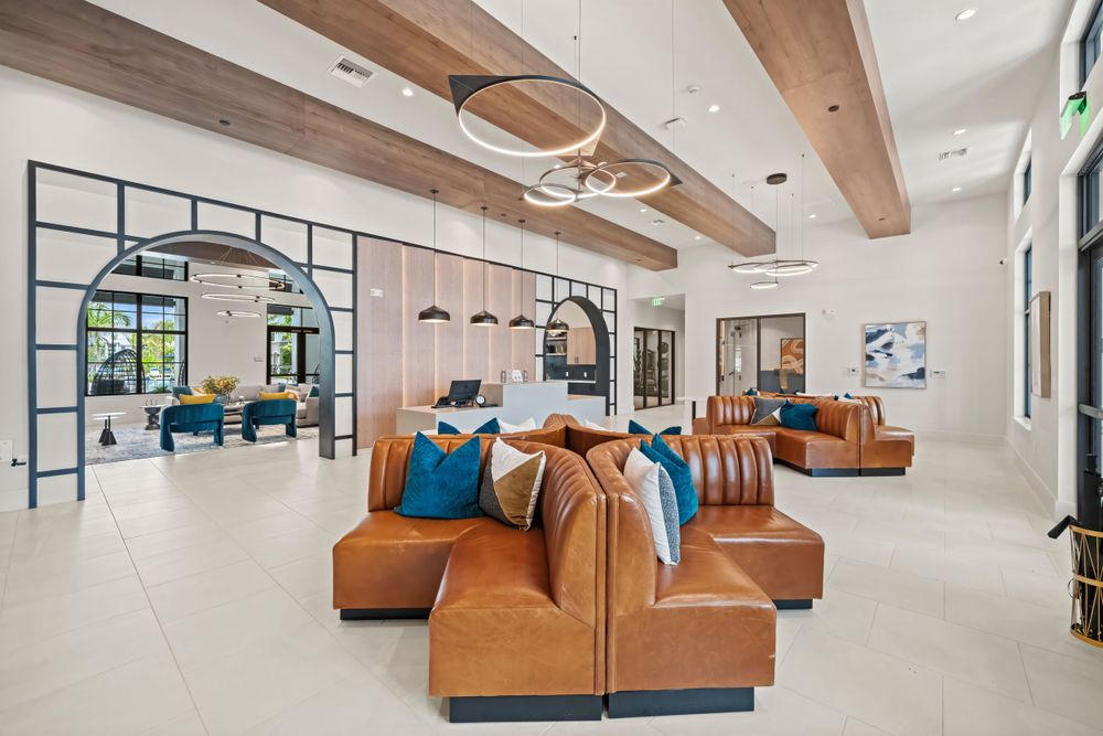 Modern lobby interior with tan leather seating, exposed wooden beams, and elegant light fixtures in an open contemporary space.