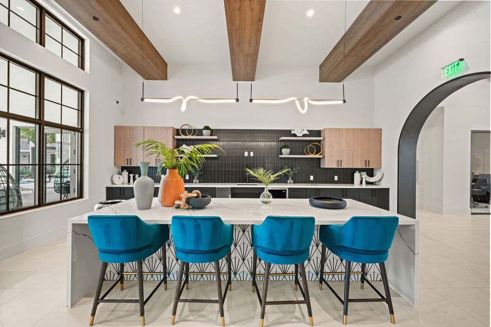 Modern kitchen featuring blue bar stools, exposed wooden beams, and a sleek white island with contemporary lighting fixtures.