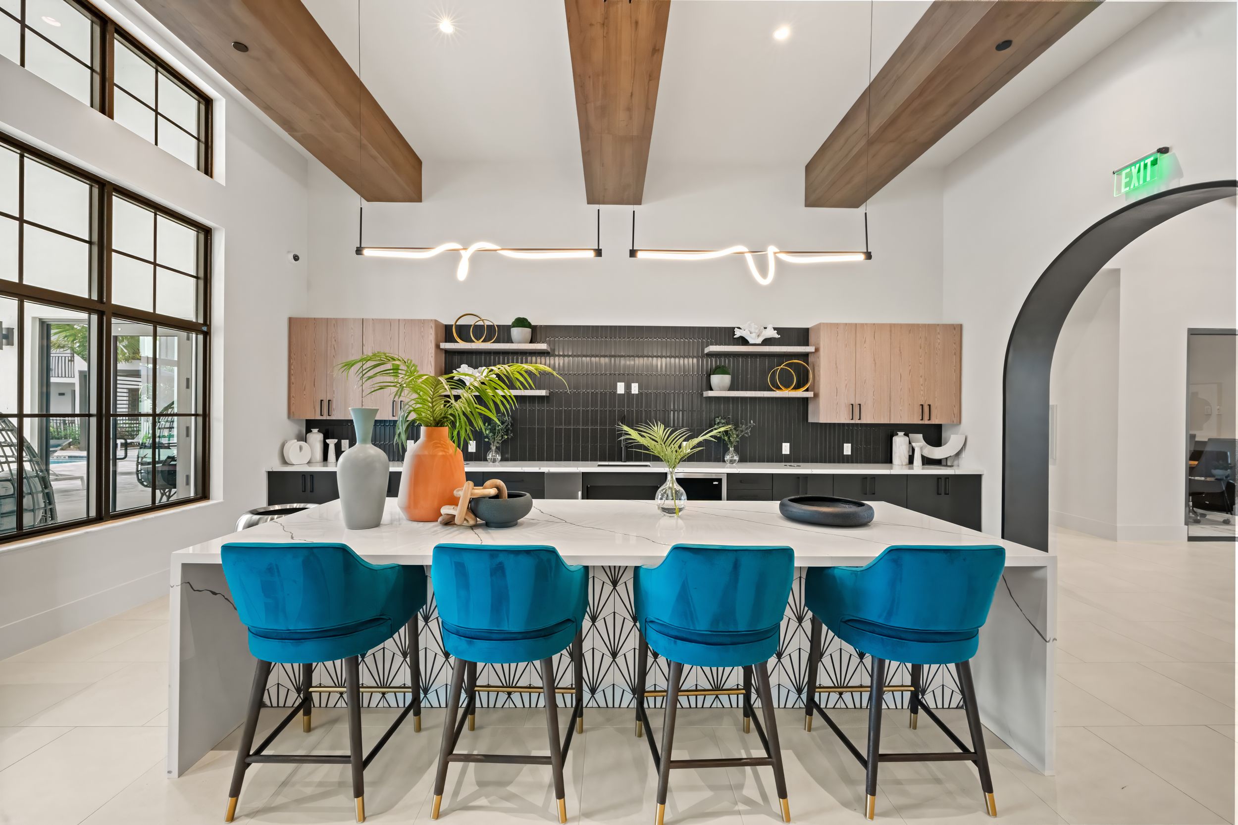 Modern kitchen featuring blue bar stools, exposed wooden beams, and a sleek white island with contemporary lighting fixtures.
