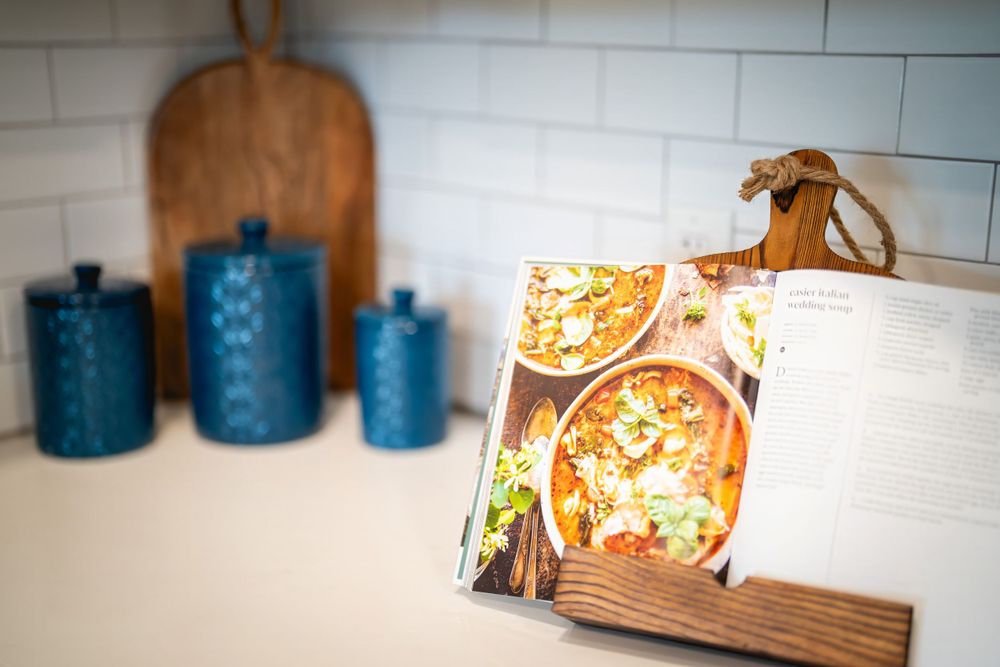 Kitchen countertop with blue ceramic canisters, wooden cutting board and a recipe book display.