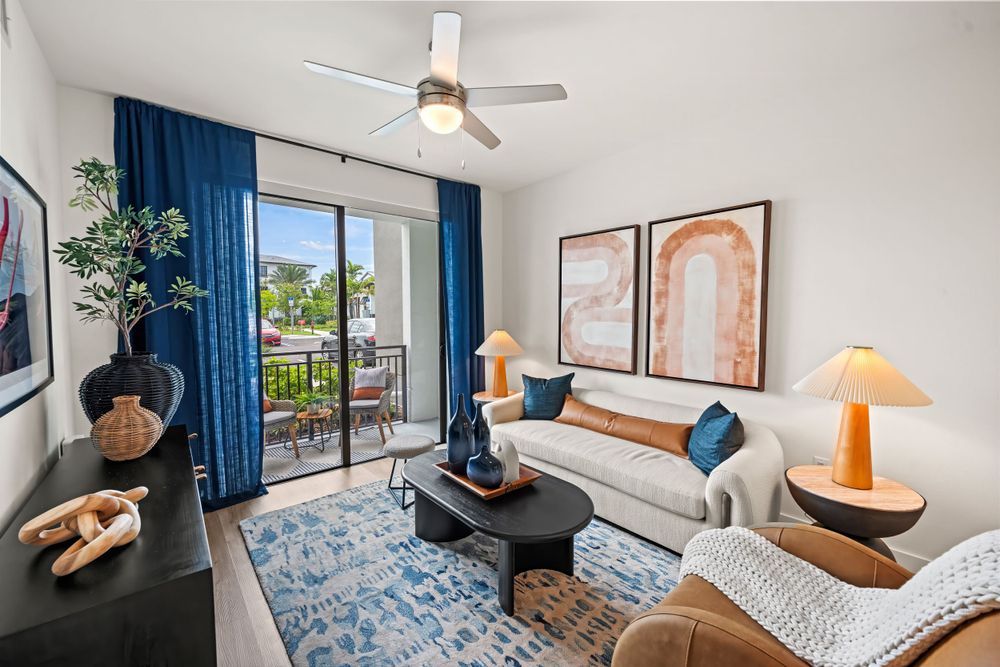 Modern coastal apartment living room with blue curtains, plush seating, and sliding door leading to a sunny balcony.