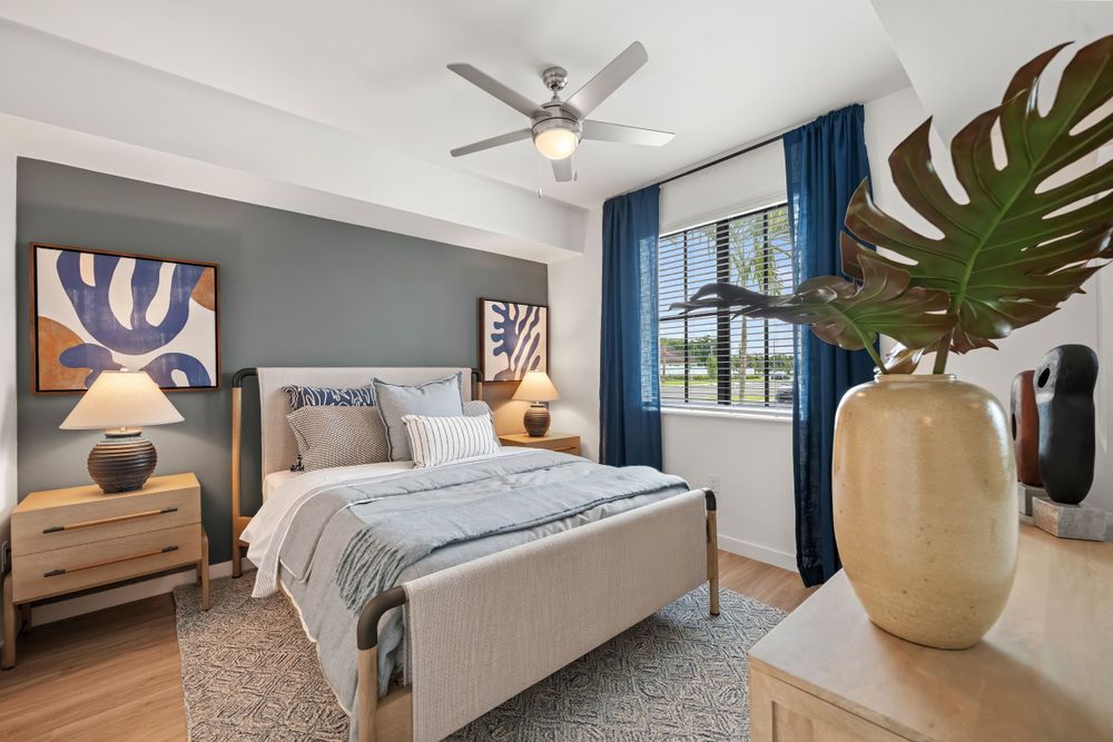 Modern bedroom with gray accent wall, blue curtains, upholstered bed, light wood furniture and decorative monstera plant.
