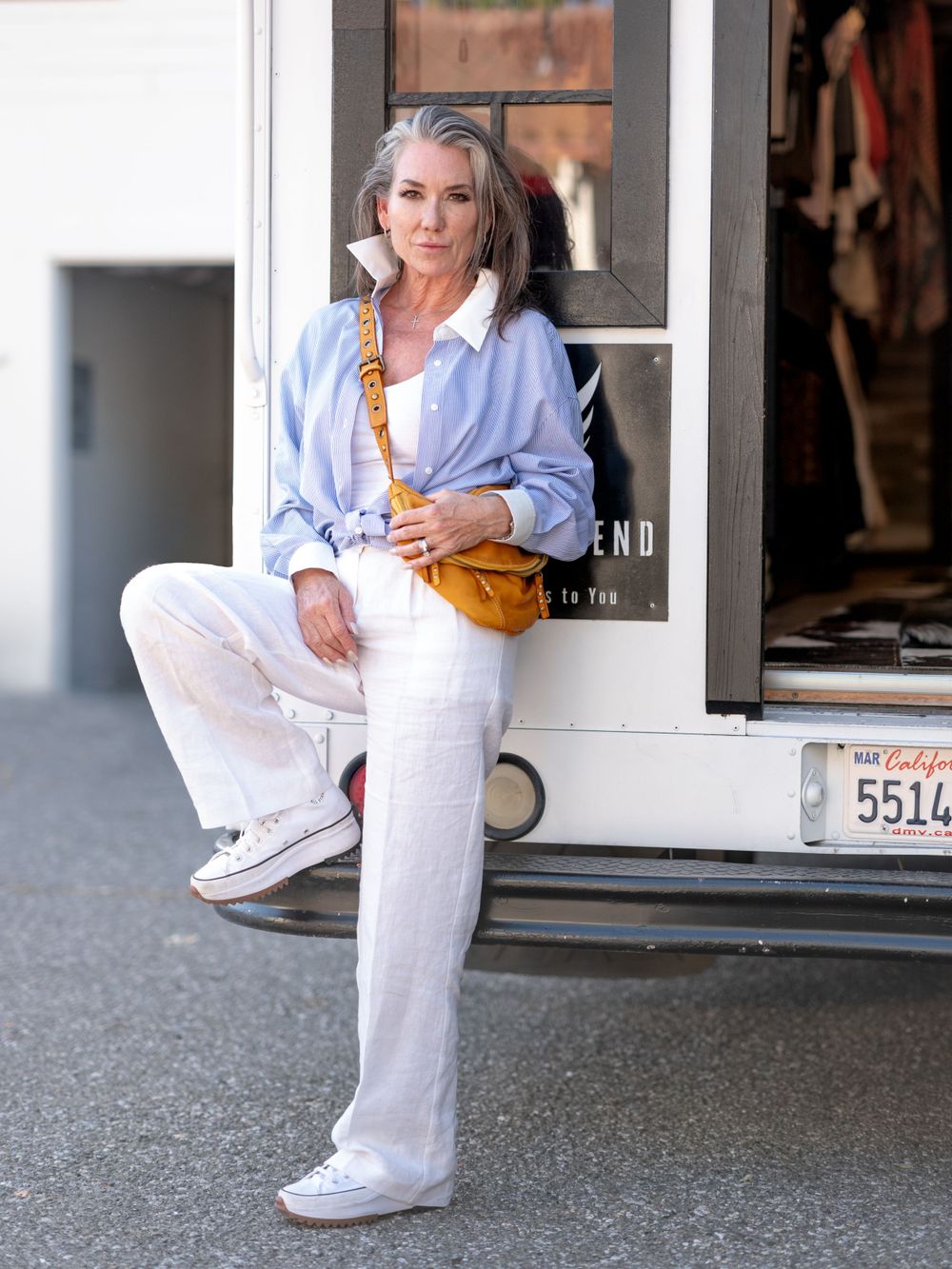 Casual chic outfit featuring light blue shirt and white pants with tan crossbody bag in fashion boutique entrance.