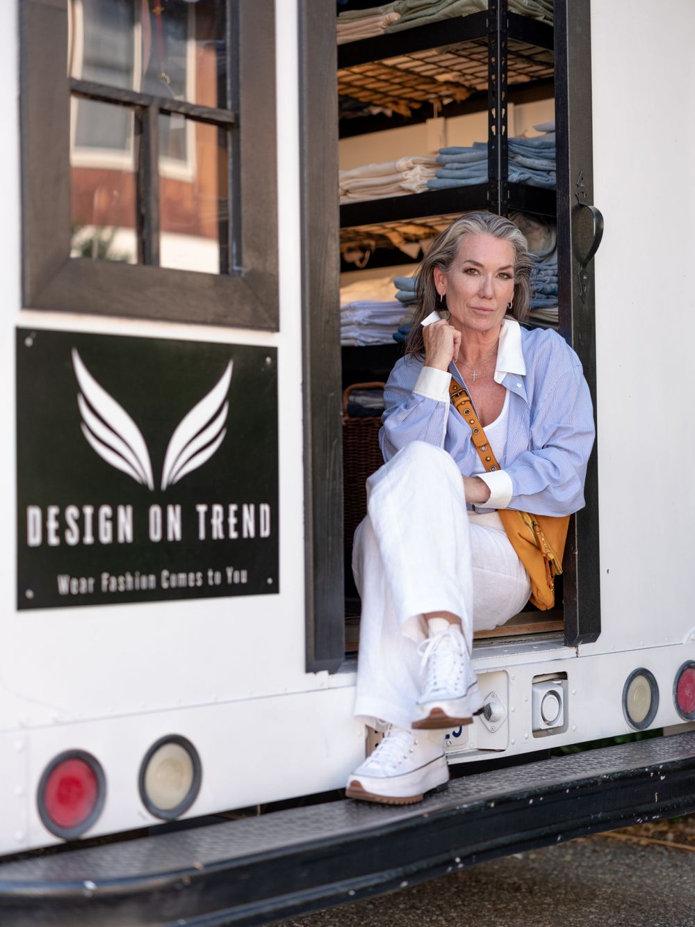 Mobile fashion boutique entrance showcasing relaxed spring style with blue shirt and white pants ensemble.