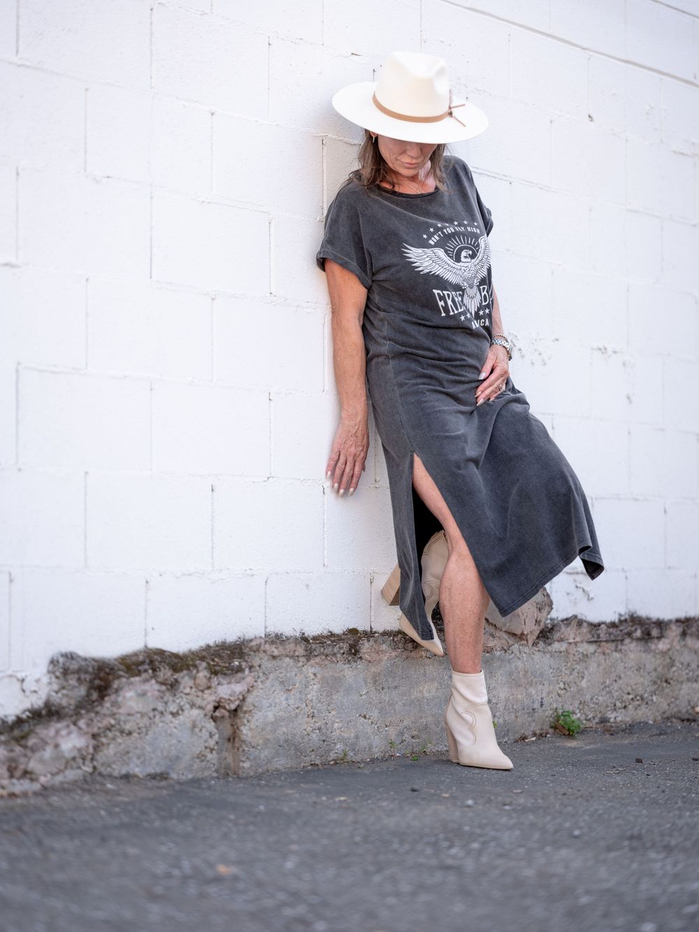 Stylish grey maxi dress paired with cream cowboy hat and ankle boots against white wall.