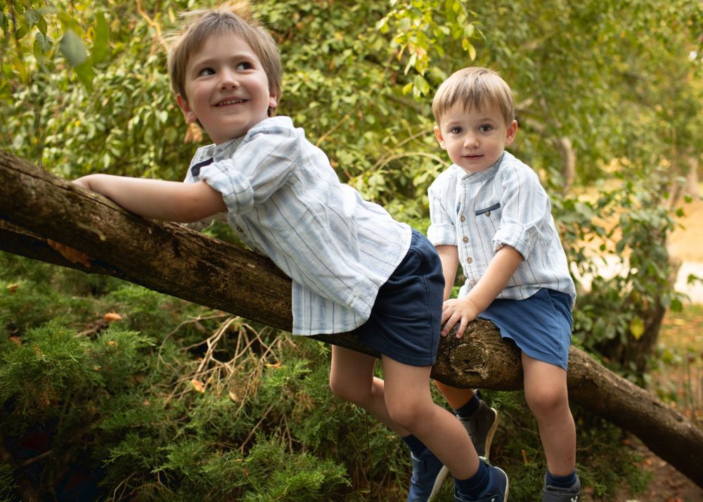 Child plays on fallen tree branch in outdoor nature setting.