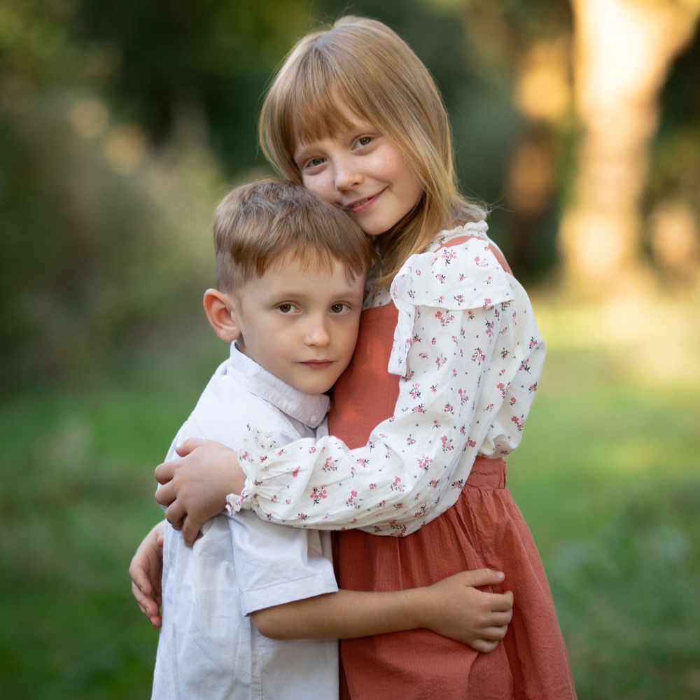 Children sharing tender moment in rustic outdoor setting during golden hour.