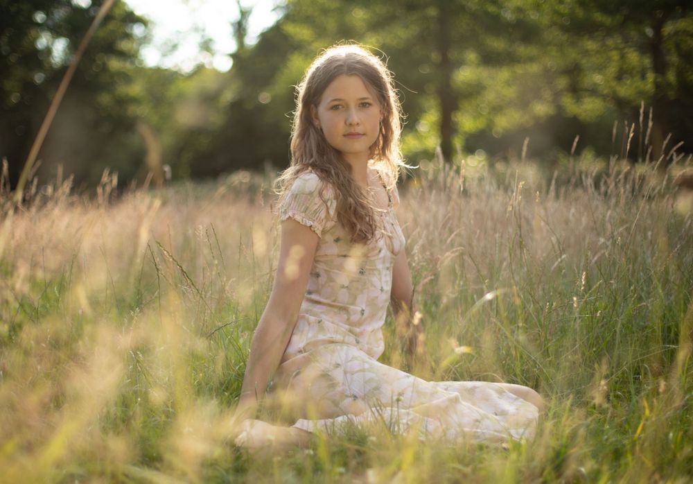 Woman in floral dress poses in sunlit meadow during golden hour.