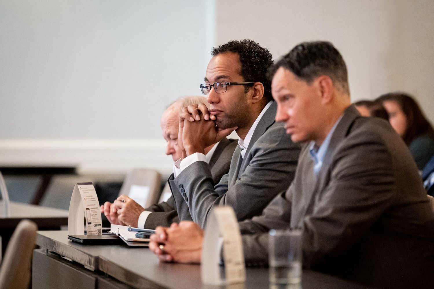 Business professionals in suits sit attentively during a corporate meeting in a conference room.