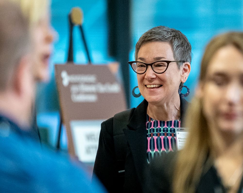 A speaker at a conference wearing glasses is shown in a sequence of candid shots with a blue backdrop.