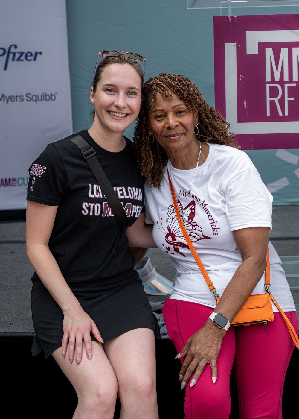 Two women smile together at a Multiple Myeloma awareness walk event with Pfizer sponsor banner.