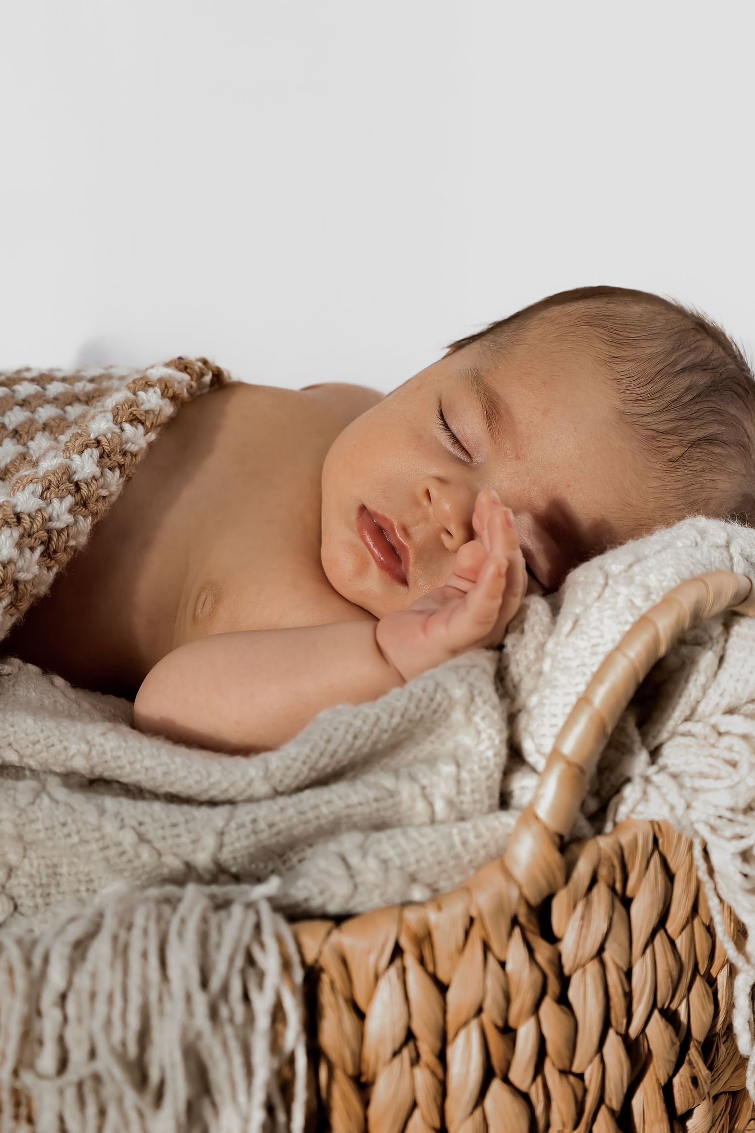 Sleeping newborn nestled in knitted blankets inside a woven basket.