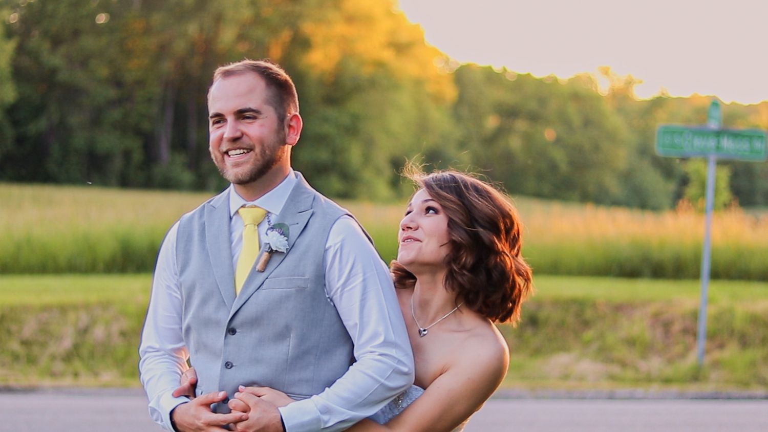 A couple shares a joyful moment together outdoors during golden hour, with her head resting on his shoulder.