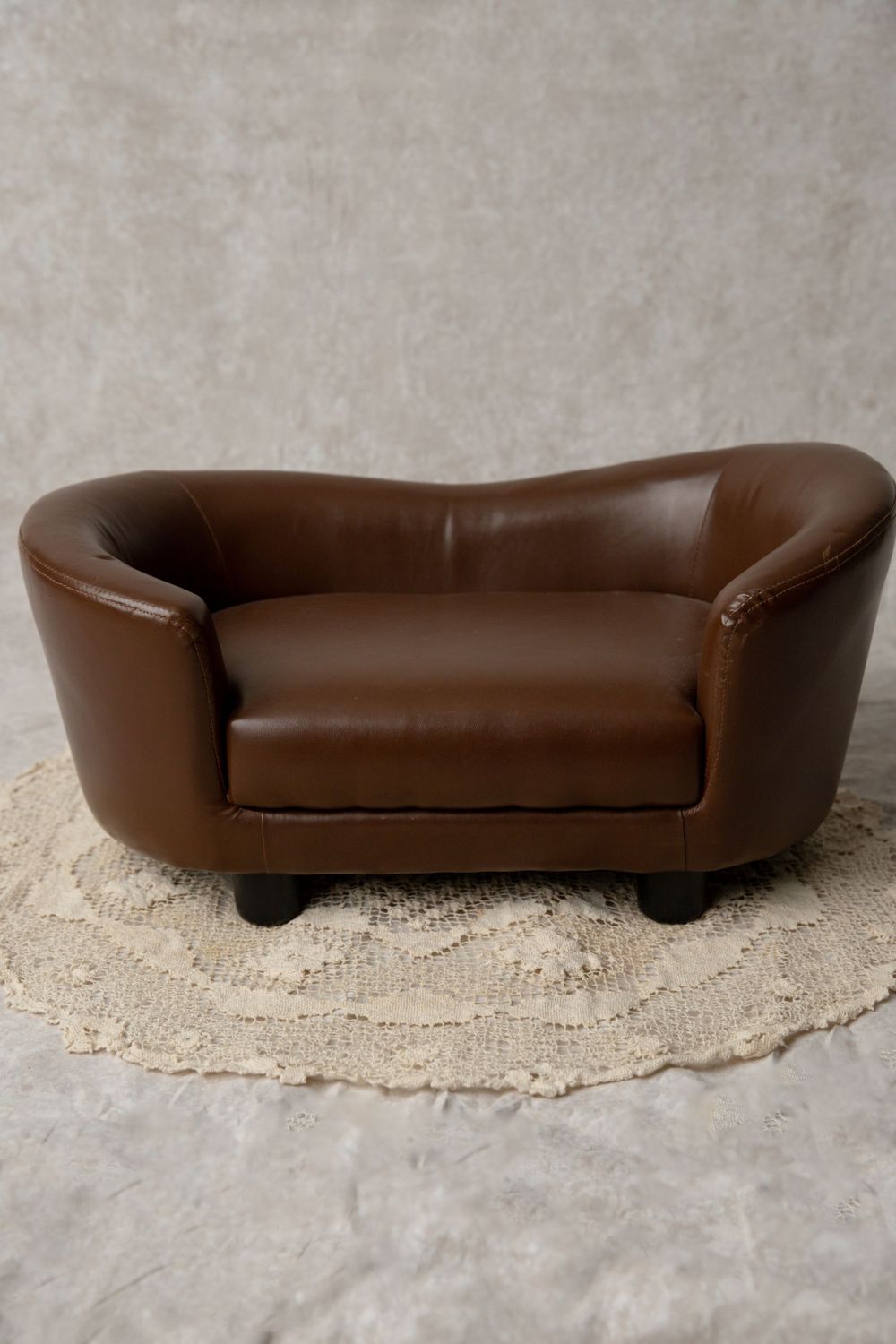 Brown leather mini loveseat prop on a cream crochet doily against a gray background.