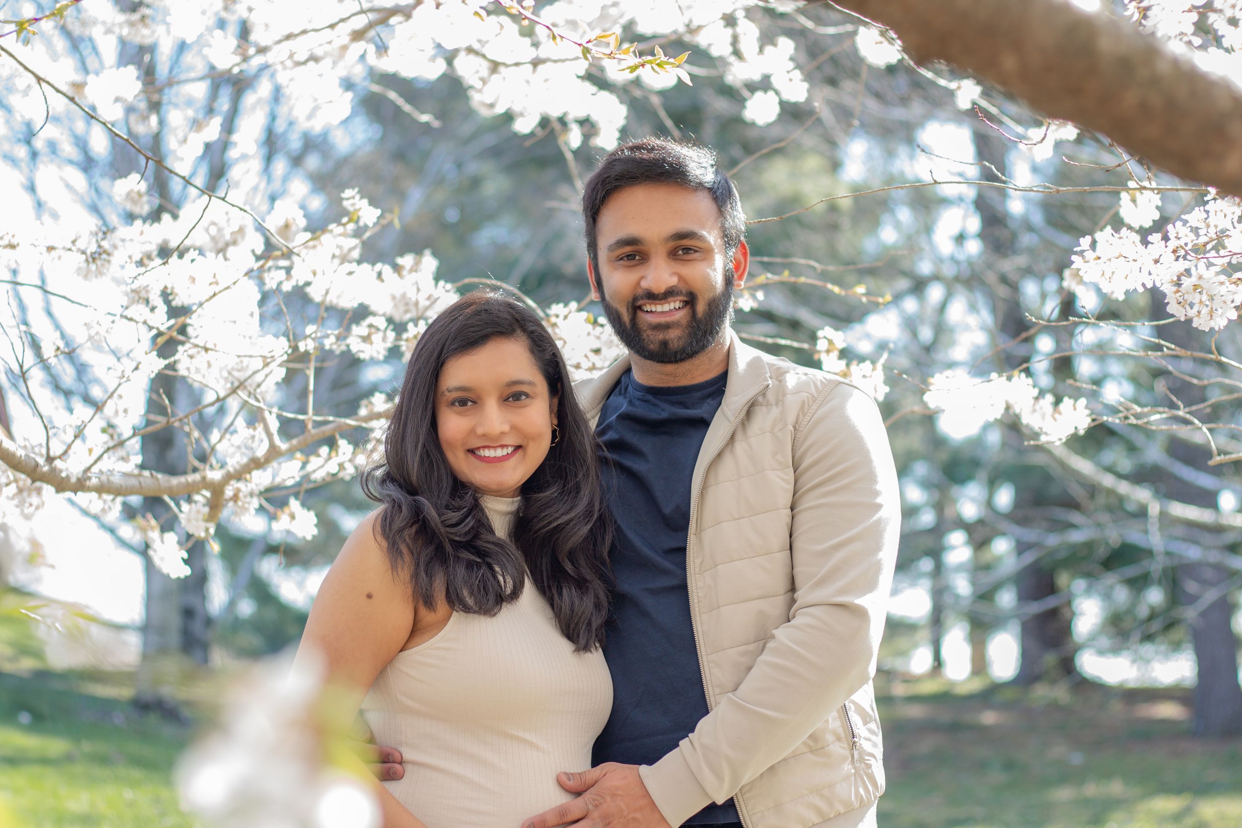 Happy couple smiling together beneath flowering white cherry blossom branches on a sunny spring day.