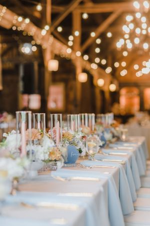 Elegant wedding reception table with soft blue linens and romantic string lights hanging in rustic barn venue.