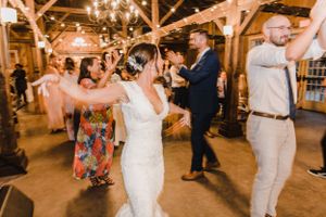 Wedding guests dancing and celebrating at a rustic barn reception venue with wooden beams and chandeliers.