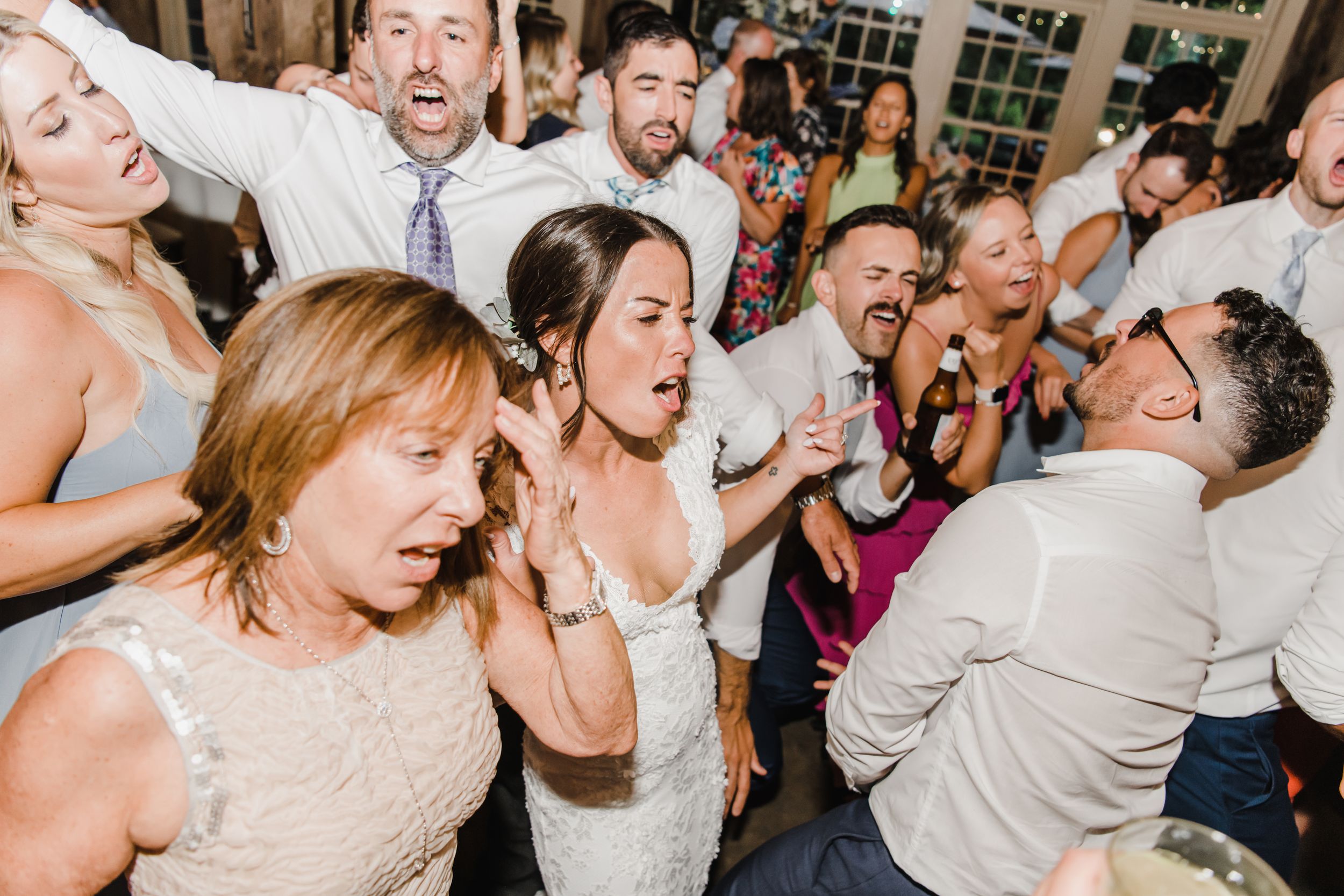 Energetic wedding reception dance party showing guests singing and dancing with pure joy and enthusiasm on the dance floor.