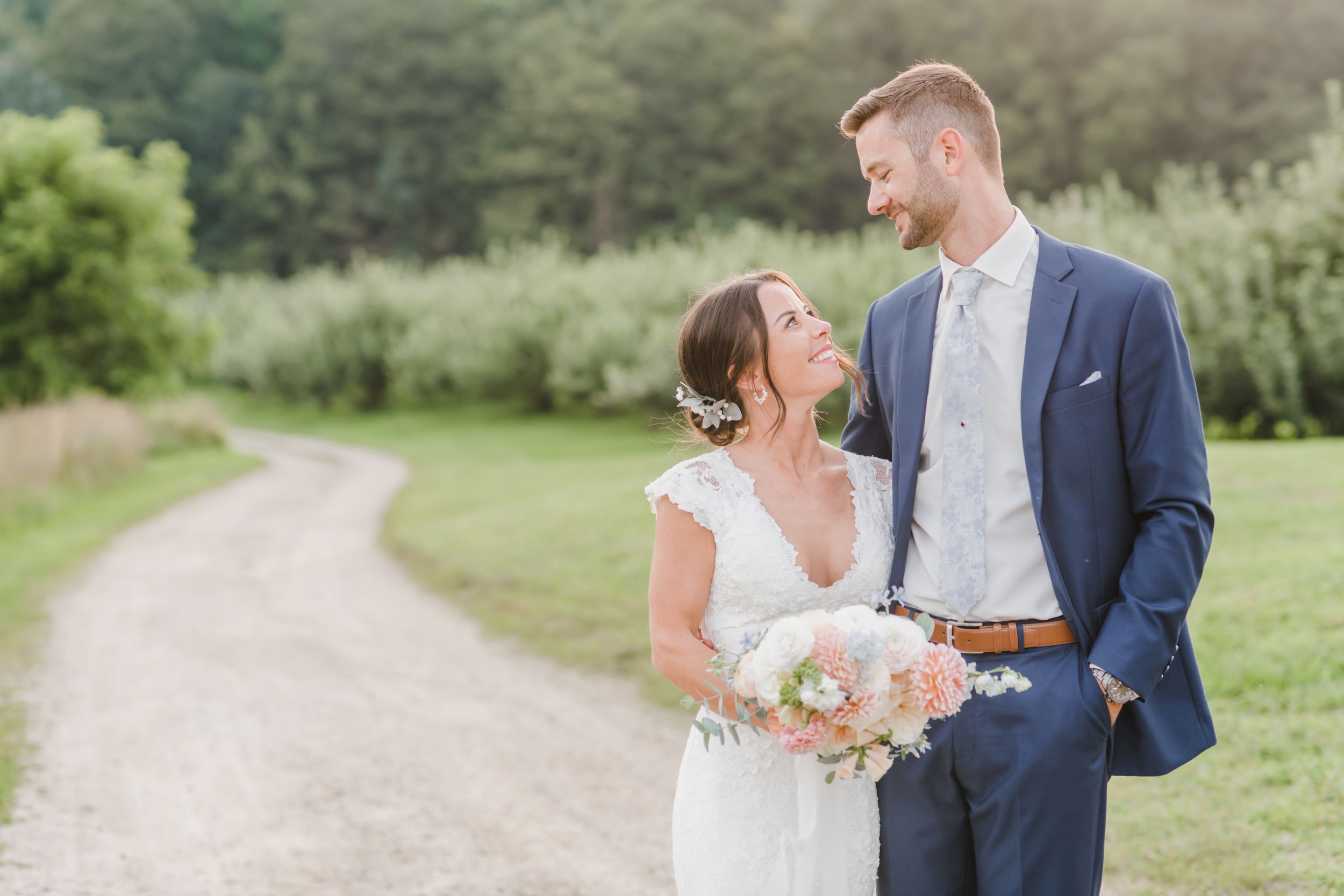 A bride and groom share a romantic moment on a winding country path surrounded by lush greenery.