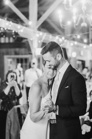 A romantic black and white photograph of a couple sharing their first dance at a wedding reception with string lights above.