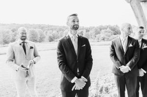 Black and white photo of groom and groomsmen standing outdoors at wedding ceremony smiling together.