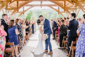 A newlywed couple shares their first kiss during an outdoor wedding ceremony under a rustic wooden pavilion.