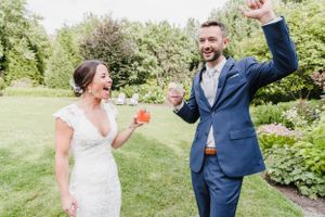A joyful couple celebrates in a garden setting, with the bride in white lace and groom in navy blue suit dancing.