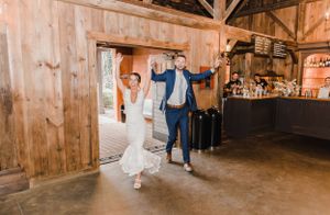 Happy couple dances together in a rustic wooden barn venue with natural lighting streaming through the entrance.