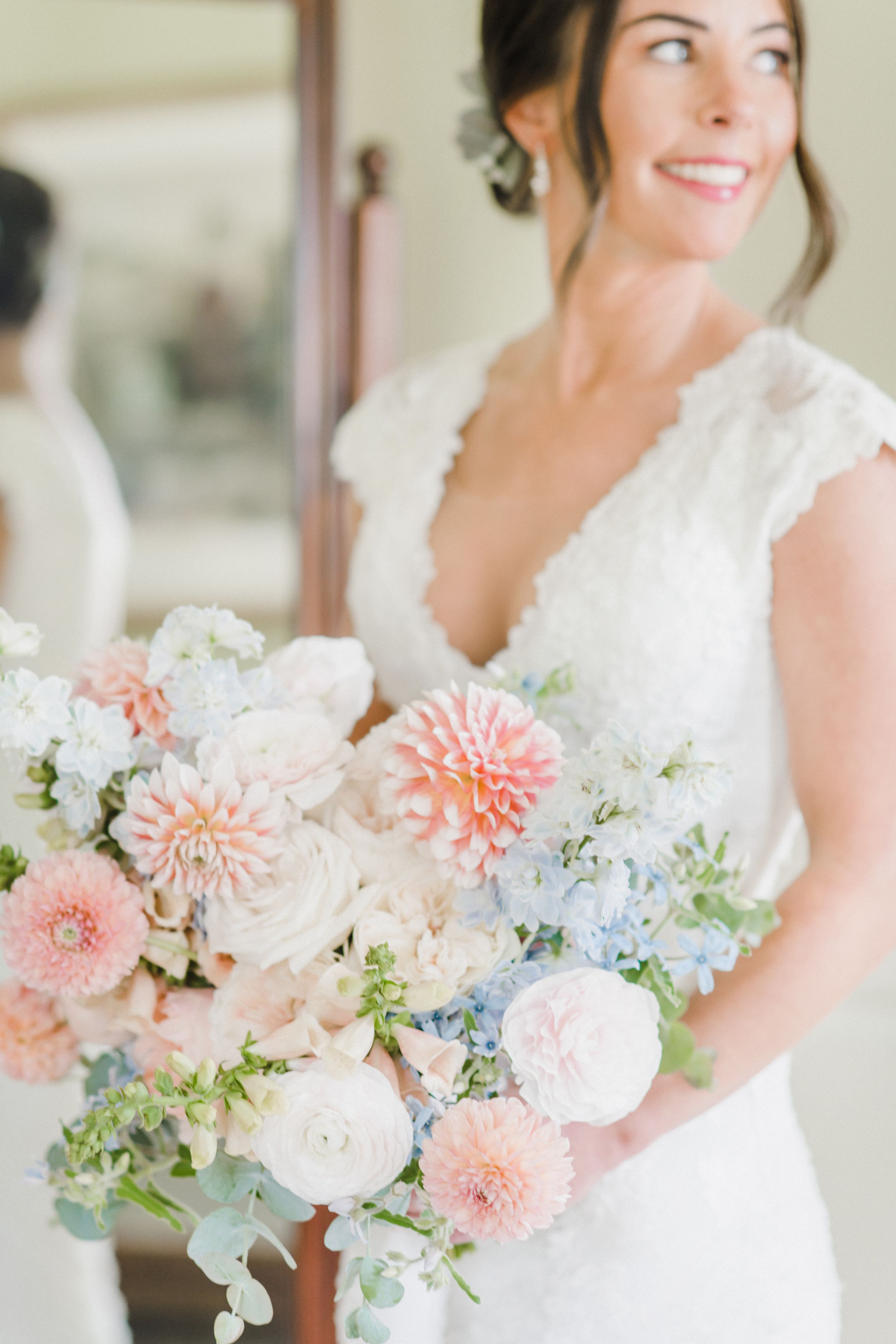 A beautiful pastel wedding bouquet with pink dahlias, white roses, and delicate greenery complements an elegant lace gown.