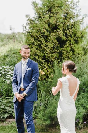 A couple in wedding attire share a moment in a garden setting with greenery and white flowers in the background.