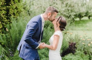 A couple in wedding attire share a tender moment in a lush garden setting with soft natural light.