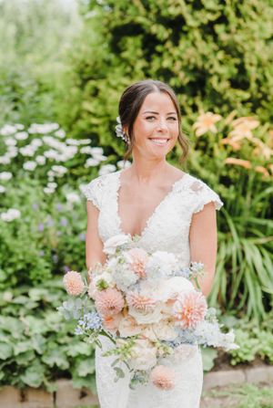 Beautiful garden wedding dress with lace details and peach and white floral bouquet among lush greenery outdoors.