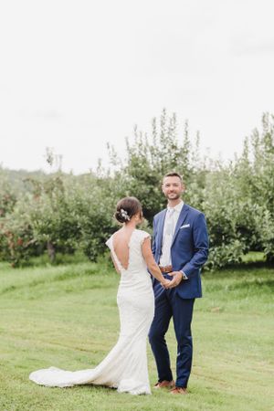 A couple in wedding attire stands together in an apple orchard on their special day.