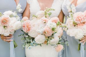Wedding bouquets featuring peach and white flowers with delicate greenery held against light blue bridesmaid dresses.