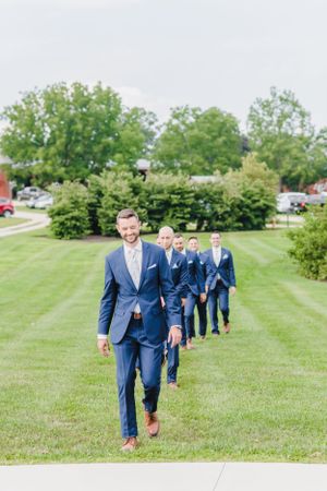 A group wearing matching navy blue suits walks in a line formation across a manicured green lawn.