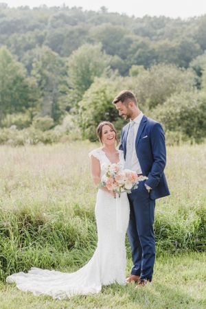 A newlywed couple shares a joyful moment together in a sunny meadow with trees in the background.