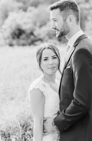 Black and white outdoor wedding portrait of a happy couple embracing in formal attire against a nature backdrop.