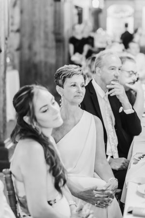 A black and white wedding reception photo showing wedding guests seated at a table in formal attire.