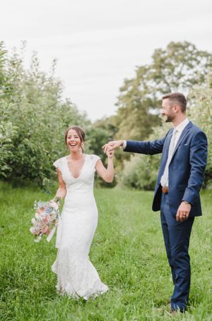 Newlyweds share a joyful moment in a lush garden setting with the bride wearing a fitted lace gown and holding a bouquet.
