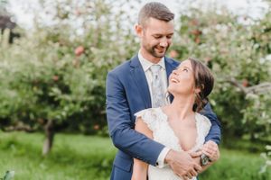A couple in wedding attire share a romantic moment in a blooming garden with red flowers in the background.