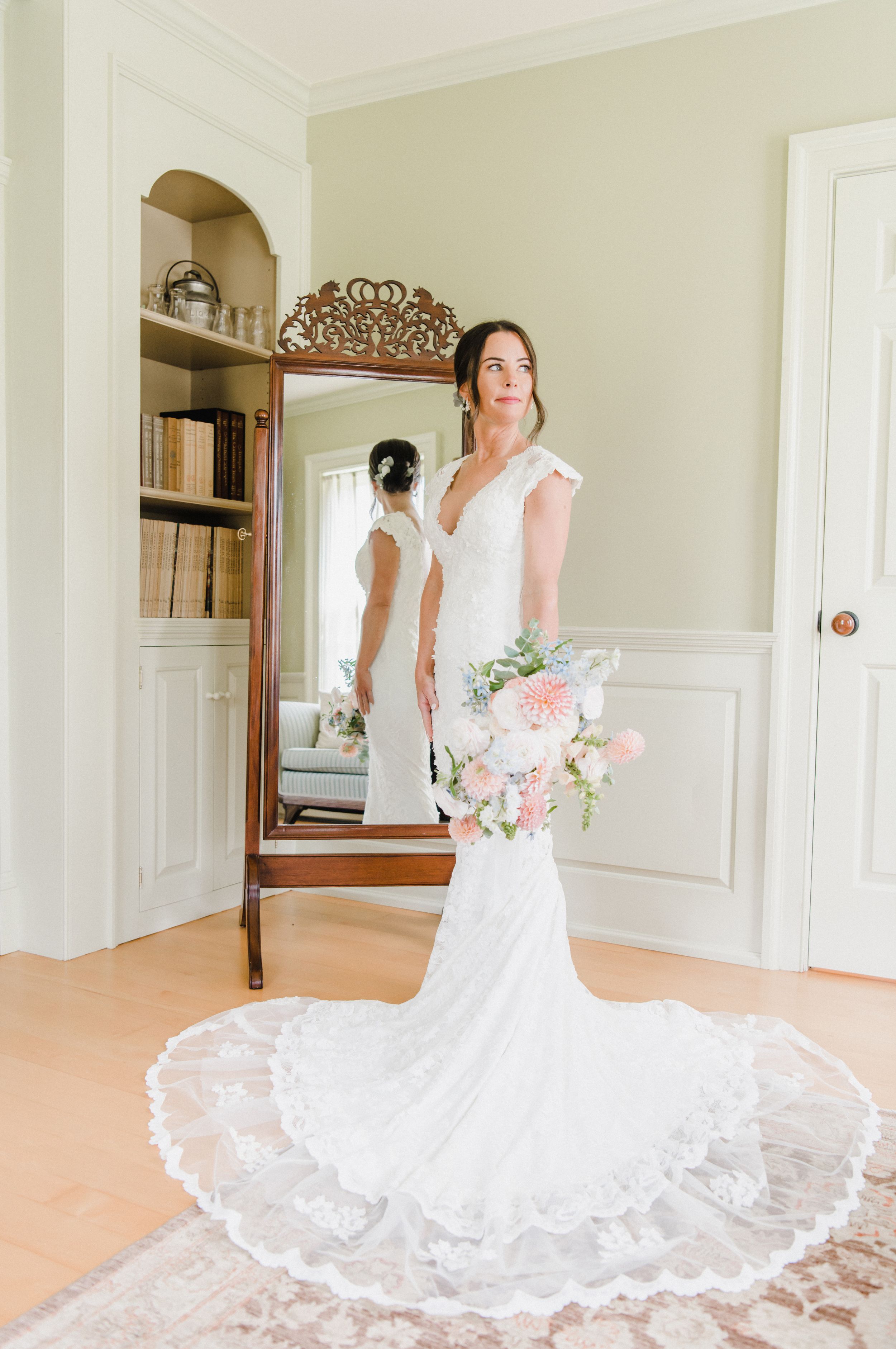 Elegant white lace wedding gown with intricate train displayed in a classic room with arched doorway and mirror.
