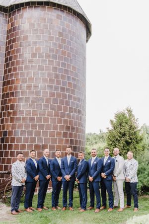 Group in navy suits and formal attire lined up against a rustic brick silo on a sunny day.