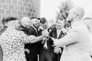 A candid black and white photo of groomsmen sharing a laugh and celebrating together at a wedding.