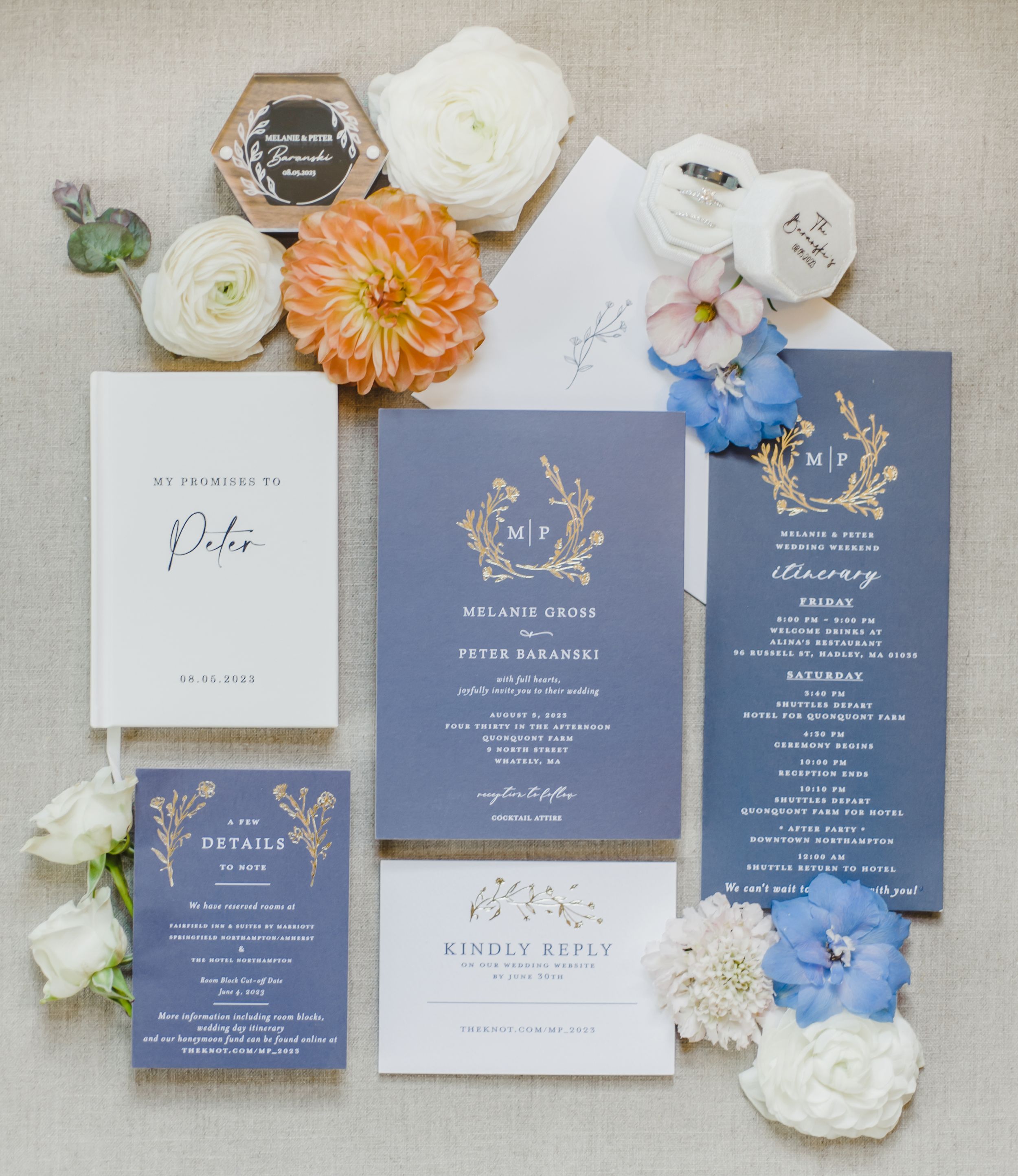 Elegant wedding invitation suite in navy blue and gold with delicate floral details surrounded by peach and white flowers.