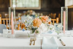 Elegant wedding table setting with peach and white floral centerpiece, gold cutlery, and soft natural lighting.