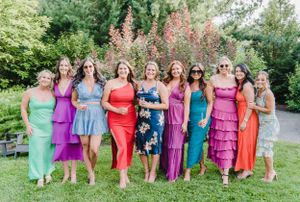 Group of people in vibrant colorful dresses stand together on green lawn in garden setting.